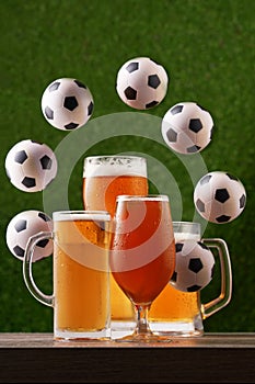 Four glasses of beer with circle frame from soccer balls on the green grass background.
