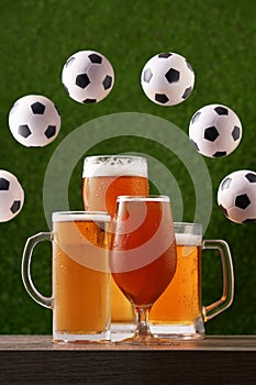 Four glasses of beer with circle frame from soccer balls on the green grass background.