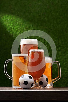 Four glasses of beer with soccer balls on the green grass background.