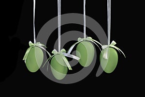 Four green Easter eggs hanging on a white ribbons with isolated on a black background.