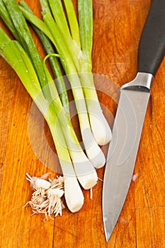 Four green onions with cut off roots and knife