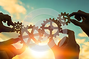 Four hands of businessmen connect gears to a puzzle on a background of sunset. Business concept idea, partnership, cooperation, te