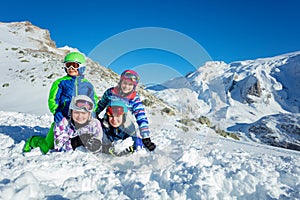 Four happy cute kids lay in snow over mountains