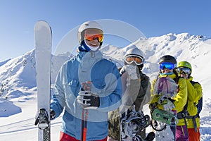 Four happy friends snowboarders and skiers are having fun on ski slope with ski and snowboards in sunny day.