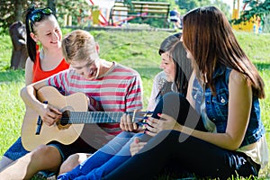 Four happy teen friends playing guitar in green summer park