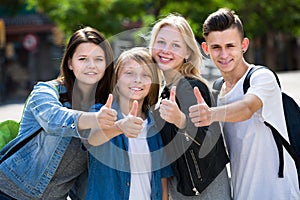 Four happy teenagers holding thumbs up together