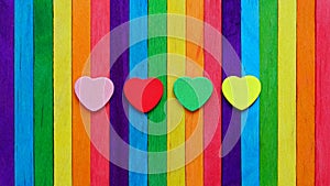 Four hearts in multiple colors on colorful ice-cream sticks line up as rainbow flag.