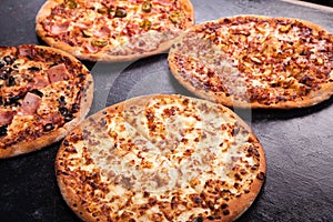 Four homemade different pizzas on dark wooden background photo
