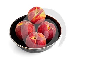Four juicy peaches in a black bowl