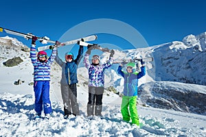 Four kids hold mountain ski in the air over sky