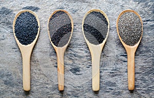 Four kinds of black organic cereal and grain seeds in wooden spoon consisted of sesame, quinoa, chia, and basil seeds