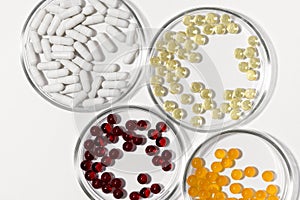 Four laboratory petri dishes with pills capsules in yellow, white, red and orange colors on a white  background.