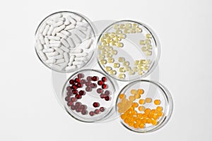 Four laboratory petri dishes with pills capsules in yellow, white, red and orange colors on a white isolated background