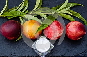 Four large peaches, a close-up of a peach sprig and a jar of cream on a black slate board.