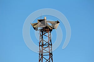 Four large public civil defence warning air sirens mounted on top of tall rusted metal structure