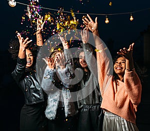 Four laughing females throw confetti in the air at night