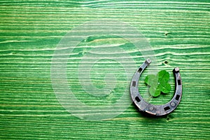 Four-leaved clover and a horse shoe on green wooden background. St. Patrick`s day