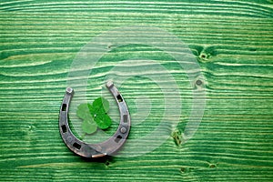 Four-leaved clover and a horse shoe on green wooden background. St. Patrick`s day