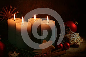 Four lighted candles for advent, Christmas decoration and gingerbread cookies against a dark brown rustic background, copy space,