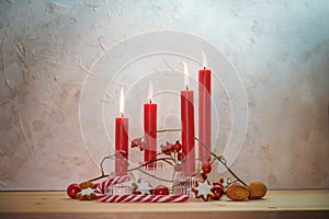 Four lit red candles for the fourth Sunday before Christmas, Advent decoration on a wooden table against a rustic wall, copy space