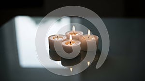 Four Lit Tea Light Candles with Reflections on Dark Surface