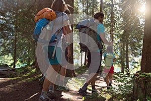 Four man and woman walking along hiking trail path in forest woods during sunny day. Group of friends people summer