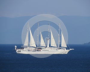 A four-mast white ship under sail moves across the blue sea