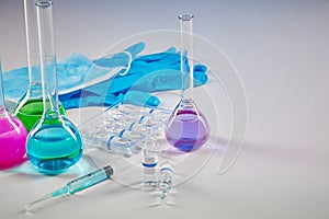 Four medical flasks with colorful chemical reagents. Seven mockup ampoules, syringe, blue disposable gloves and mask