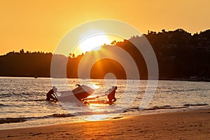 Four mens at sunset pull hydrocycle out of the water. Workers of the beach. Water bike loaded onto a rickshaw trailer