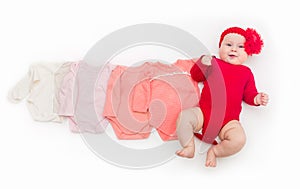 A four month happy baby in red bodysuit lying on a white background with pink clothes smaller size.