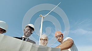 Four multi ethnic partners in safety helmets studying wind turbine blueprints while. Engineer Discussing Wind Turbines