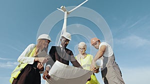 Four multi ethnic partners in safety helmets studying wind turbine blueprints while. Engineers explores future wind