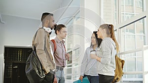 Four multi-ethnic studens are standing in big white spacious hall in college talking to each other in positive way. They