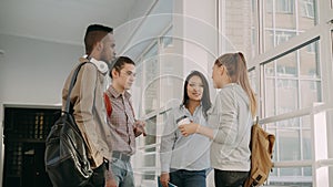 Four multi-ethnic studens are standing in big white spacious hall in college talking to each other in positive way. They