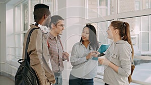 Four multi-ethnic studens are standing in big white spacious hall in college talking to each other in positive way. They