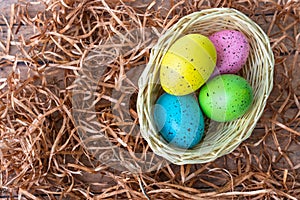 Four multicolor Easter eggs in a basket on wooden background. Easter celebratory wallpaper with copy space