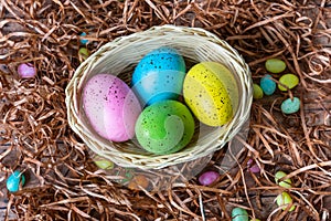 Four multicolor Easter eggs in a basket on wooden background. Easter celebratory wallpaper with copy space