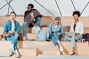 Four multicultural students with notebooks and laptop studying