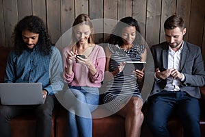 Four multiethnic people sit together indoor using diverse electronic devices