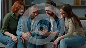 Four multiracial friends business people use smartphone look at mobile phone screen together 30s middle-aged users