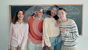Four multiracial happy students standing at black board in classroom.