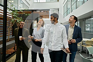 Four multiracial young adults in businesswear walking and laughing in corridor of office