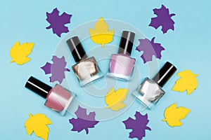 Four nail polish bottles with paper leaves decoration on blue background. Nail polish bottles with autumn leaves decoration. Nail
