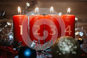 Four numbered red advent candles with first candle lit and christmas decoration lying in snow as template