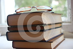 Four old books and eyeglasses near window. Knowledge education concept