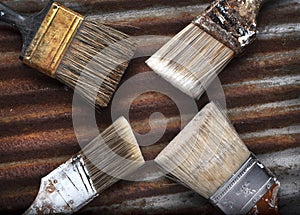 Four Old Dirty Crusty Household Paintbrushes on Rusted Corrugated Metal Background
