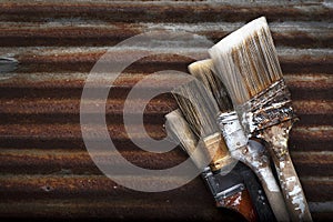 Four Old Dirty Crusty Household Paintbrushes Stacked on Each Other Rusted Corrugated Metal Background