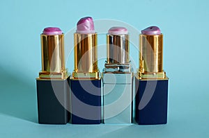 Four old used tubes of lipstick stand on a blue background.