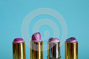 Four old used tubes of lipstick stand on a blue background.