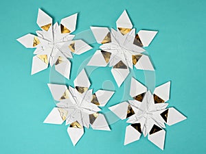 Four origami star snowflakes in white and gold foil paper, on a taupe blue paper background